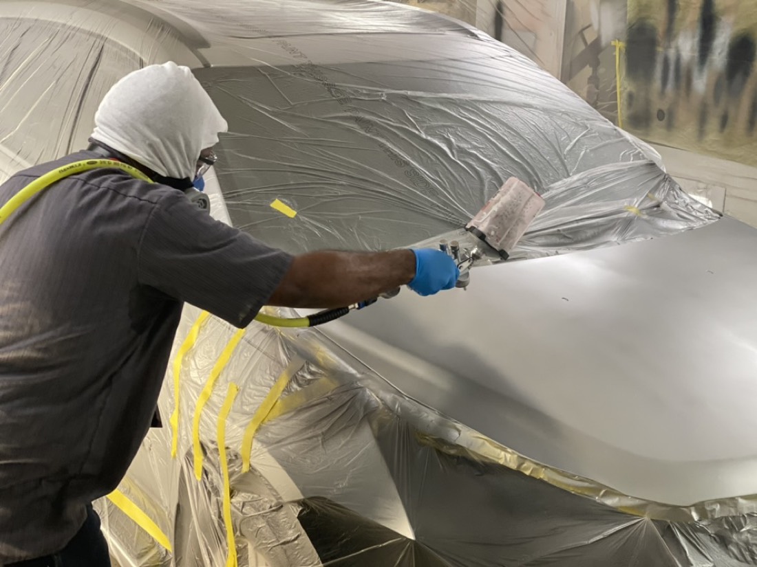 Technician in full PPE spraying with a flagship spray gun inside a paint booth